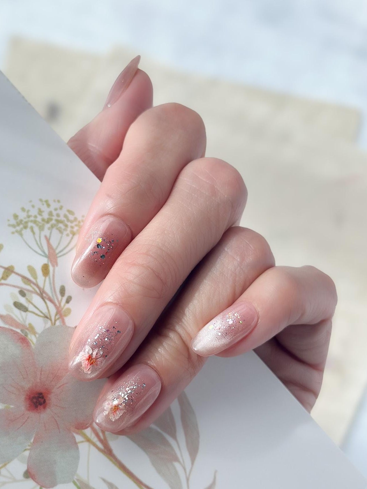 Hand with press on nail made with real dried flowers encased in a translucent blush base with fine glitter