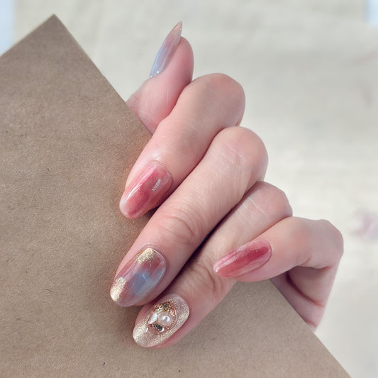 Hand with Pink and blue marble press-on nails with gold shimmer accents and pearl crystal embellishment