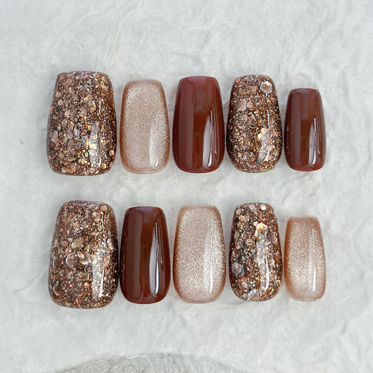Brown and gold press-on nails with glossy chocolate brown polish, champagne shimmer, and gold glitter accent nails