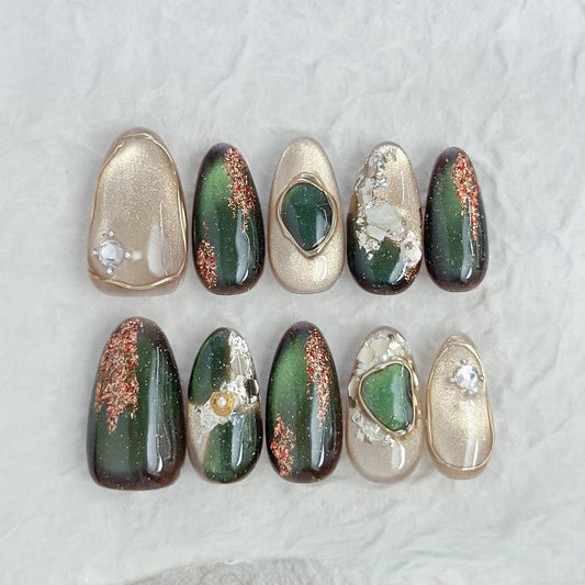Green and gold gemstone-inspired press-on nails with cat-eye shimmer, glitter accents, gold foil detailing, and 3D crystal embellishments