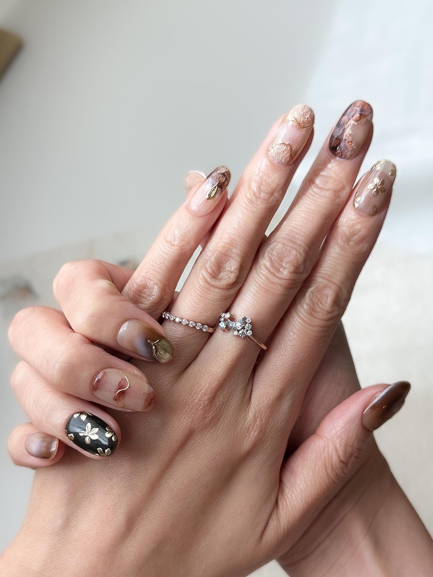 Hand with press-on nails in neutral tortoise design and mocha tones with gold foil accents, marble detailing, and embossed metallic floral designs