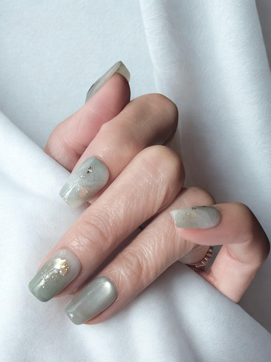 Hand with Mint green press-on nails with pearlescent shimmer, marble accents, gold foil, and tiny pearl embellishments