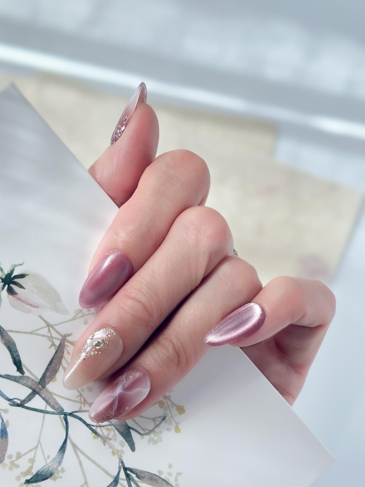 Hand with Pink and mauve press-on nails with marble design, cat eye shimmer finishes, and gold foil detailing