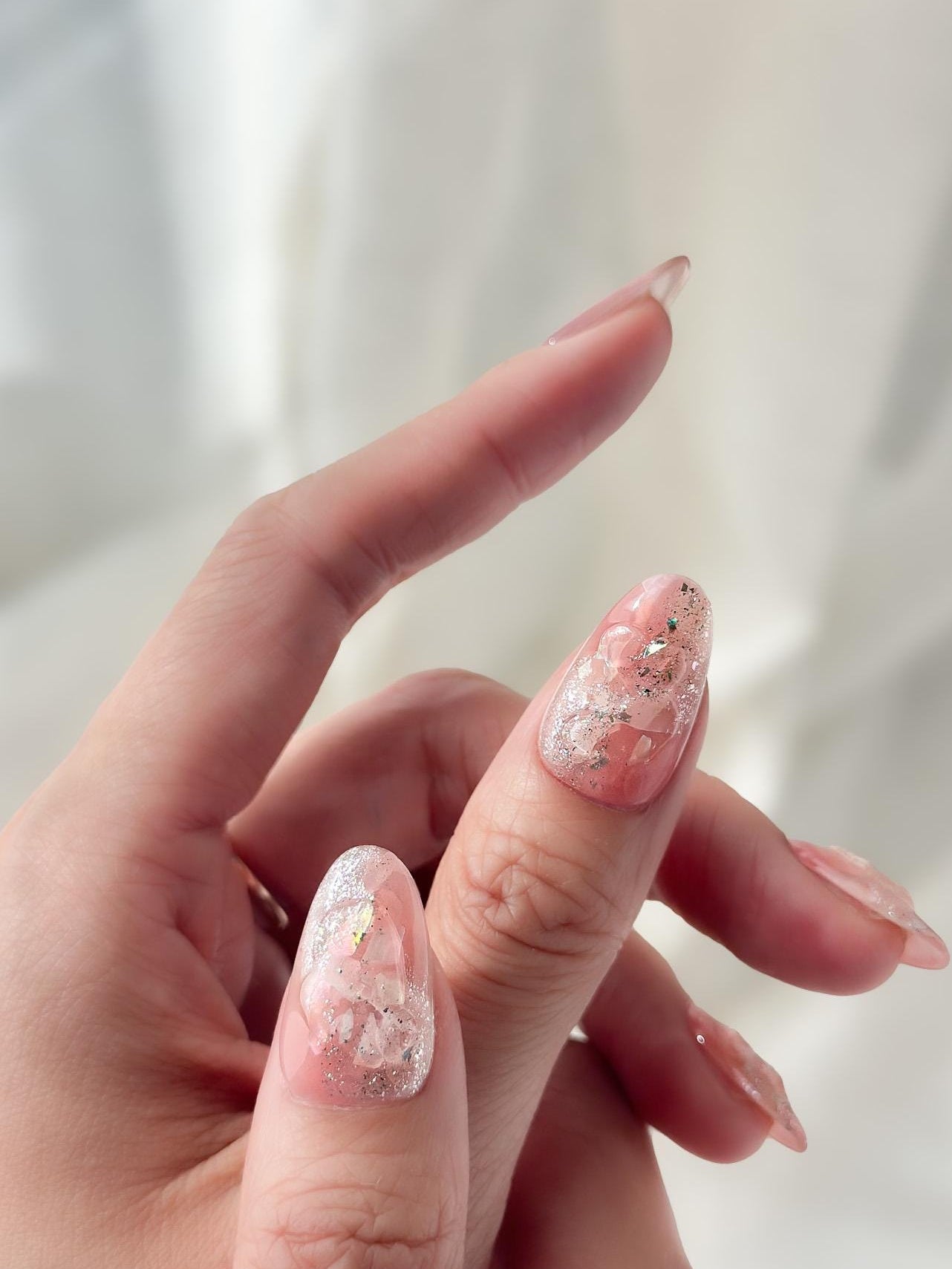 Hand with Pink shimmer press-on nails with iridescent glitter, marble swirl accents, and gold foil details