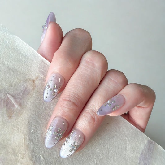 Hand with press on nails in light purple and nude ombre base with gold floral accents