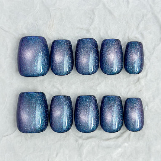Short square shaped cat-eye press-on nails in shifting blue, purple, and teal galaxy shimmer