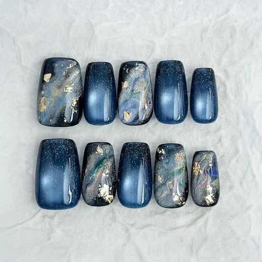 Luxury blue cat-eye press-on nails with galaxy shimmer and abstract marble accents in green, gold, and silver foil