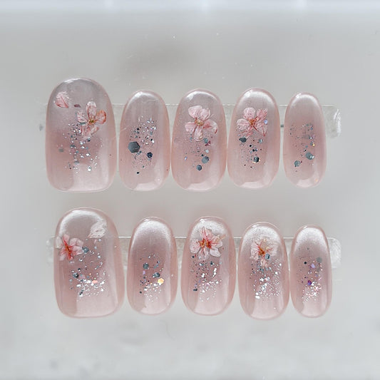 Press on nail made with real dried flowers encased in a translucent blush base with fine glitter
