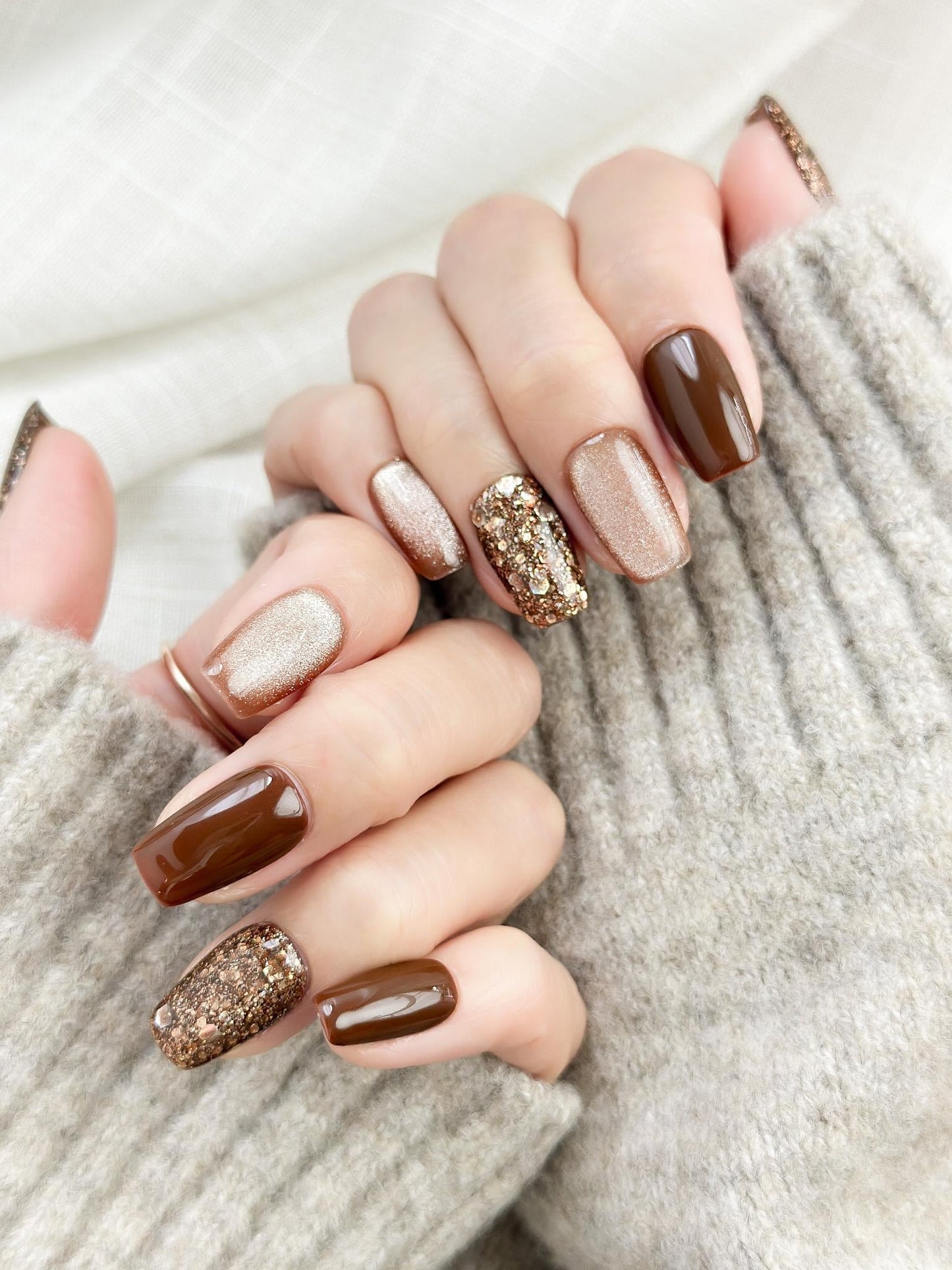 Hand with Brown and gold press-on nails with glossy chocolate brown polish, champagne shimmer, and gold glitter accent nails