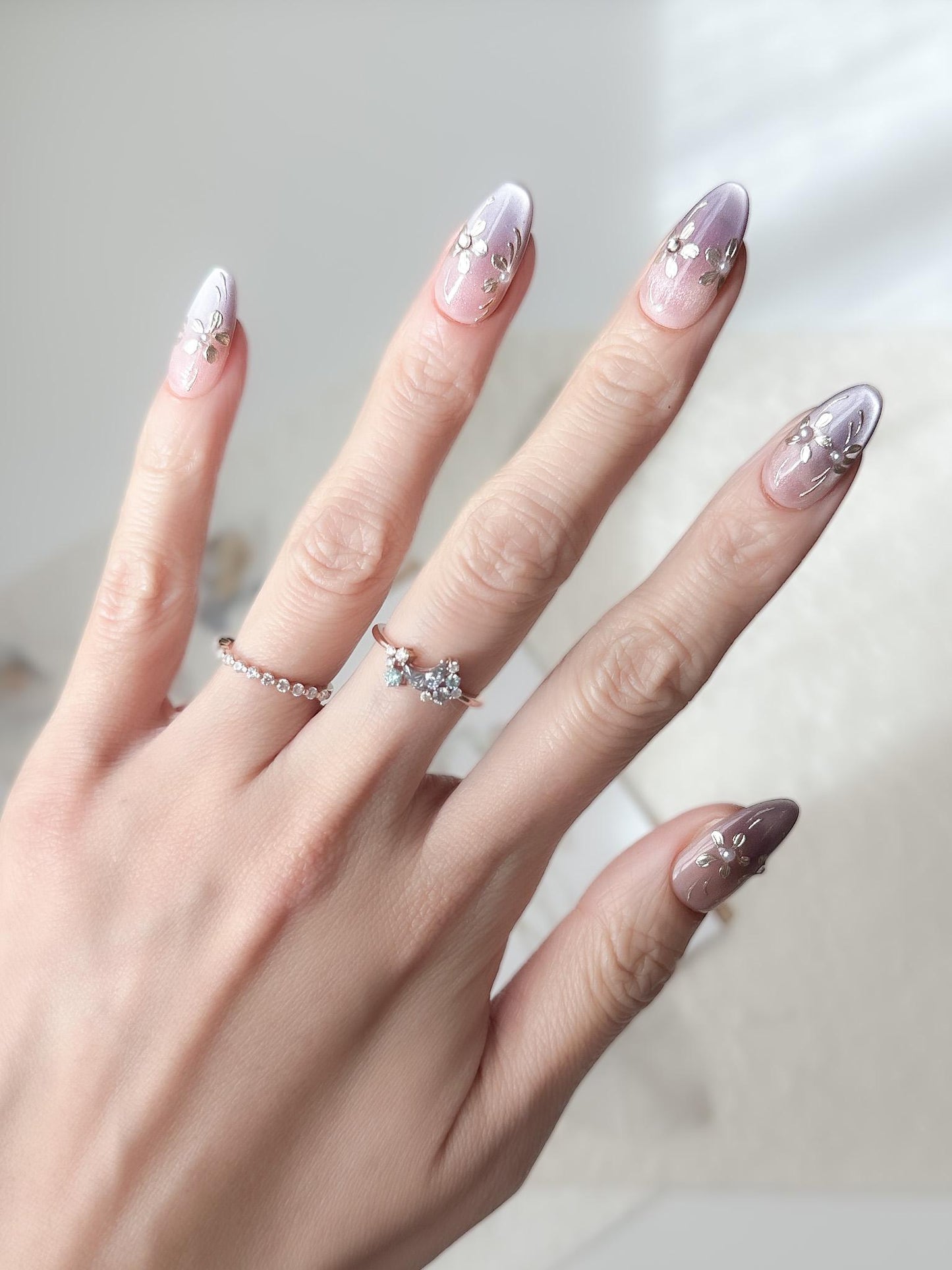 Hand with press on nails in light purple and nude ombre base with gold floral accents