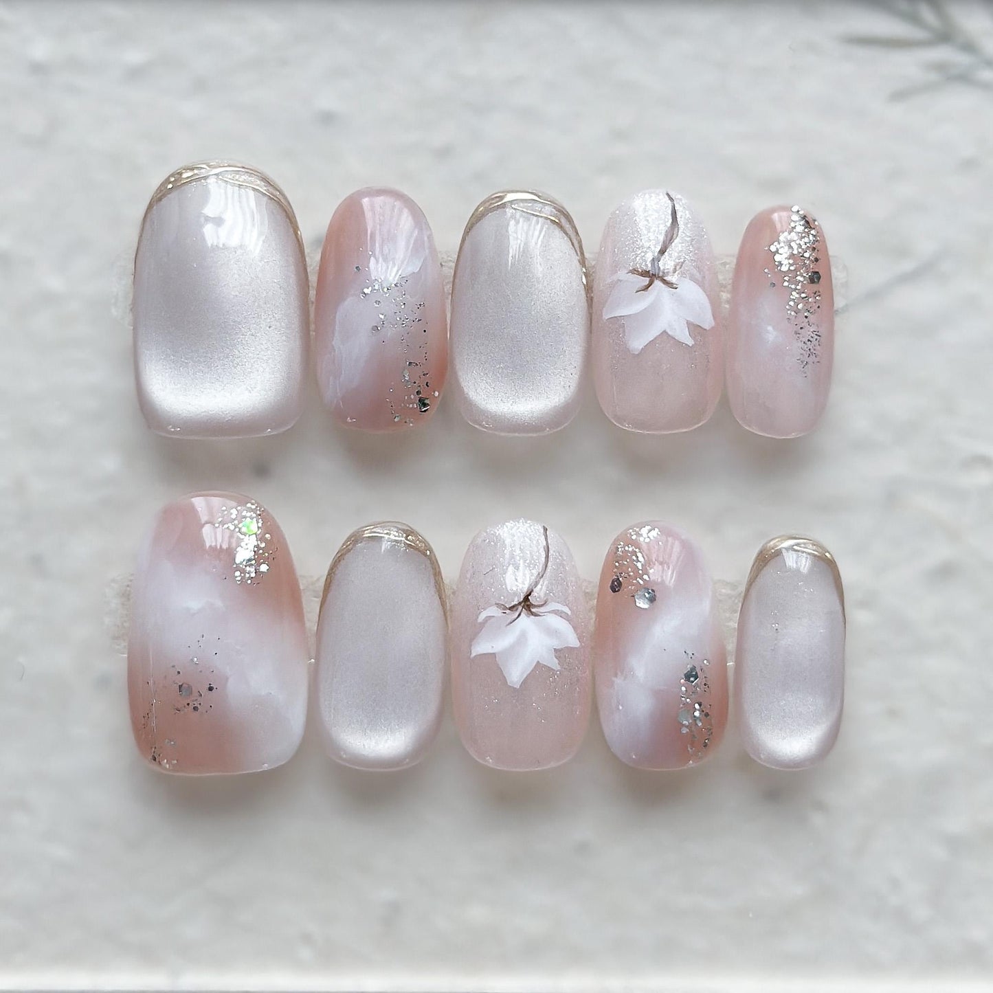 Pink and pearl white press-on nails with soft marble accents, hand-painted white floral art, silver glitter details, and glossy finish