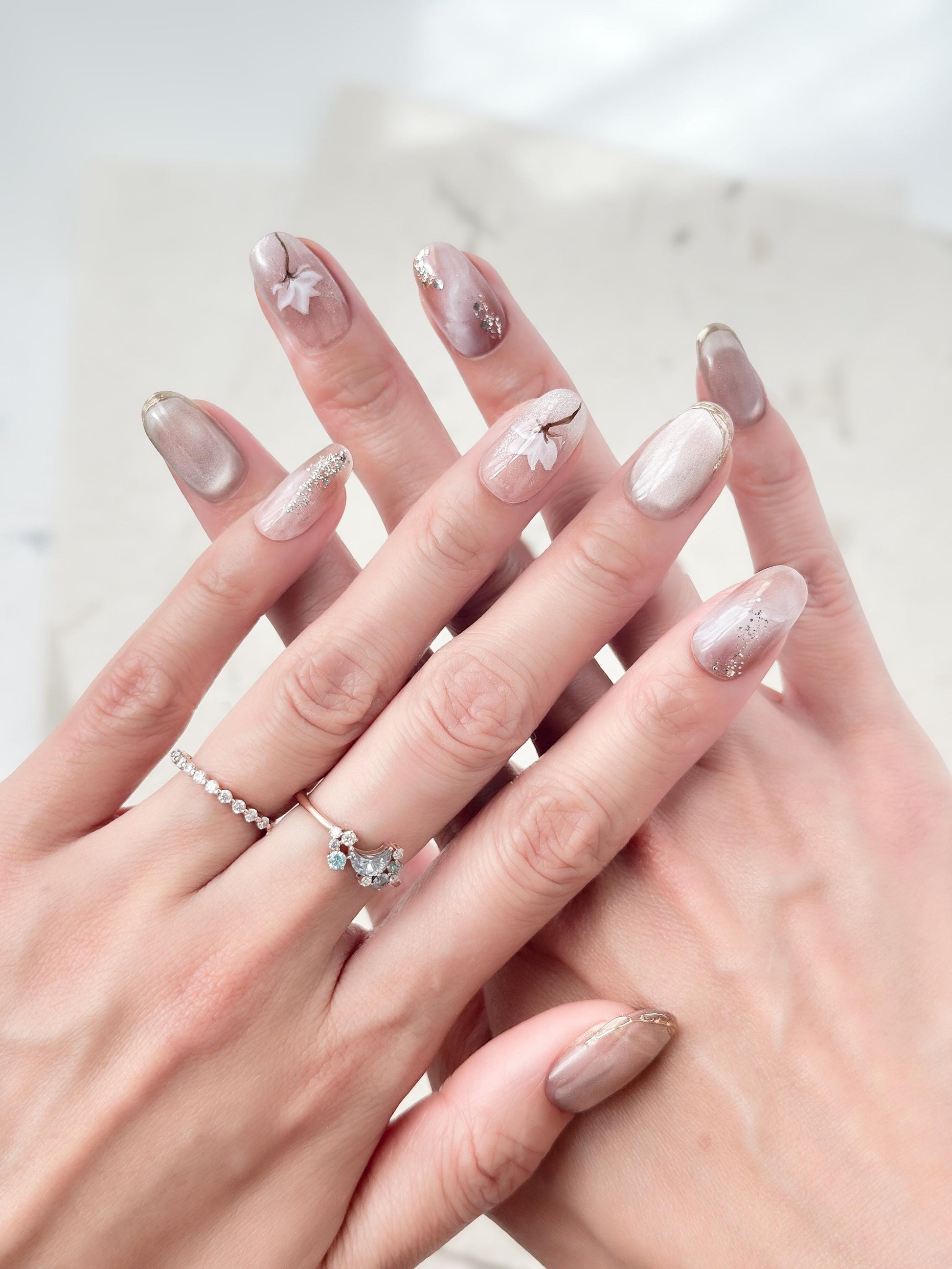 Hand with Pink and pearl white press-on nails with soft marble accents, hand-painted white floral art, silver glitter details, and glossy finish