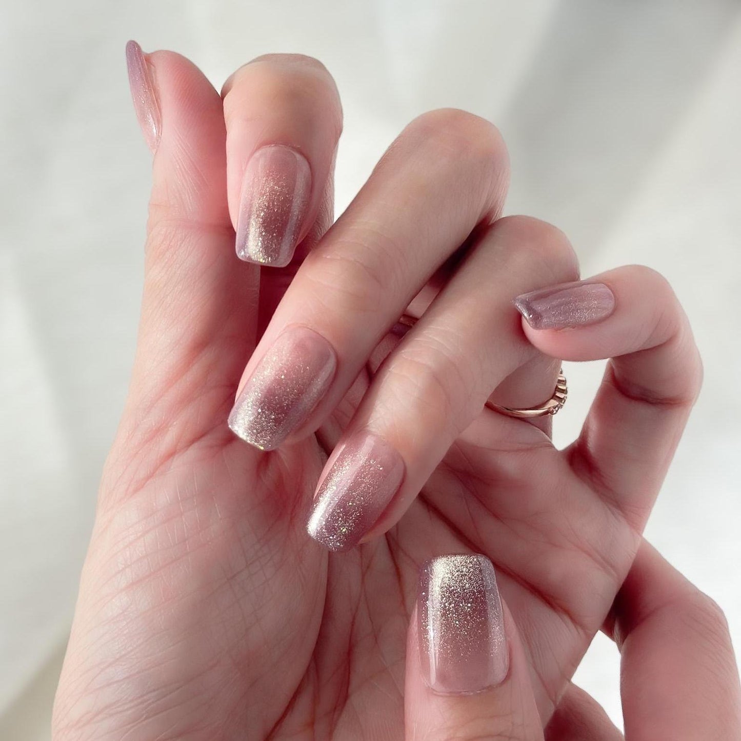 Hand with Short square pink mauve ombré press-on nails with fine glitter shimmer, soft blush gradient, and glossy finish