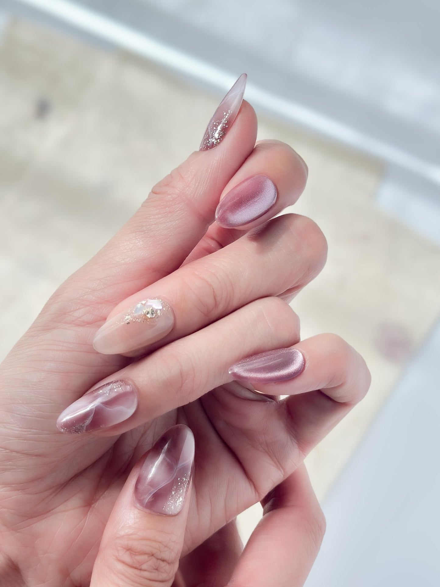 Hand with Pink and mauve press-on nails with marble design, cat eye shimmer finishes, and gold foil detailing