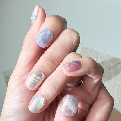Hand with Pastel celestial press-on nails with pink, lavender, and blue marble swirls, gold star accents, and a gold crescent moon design