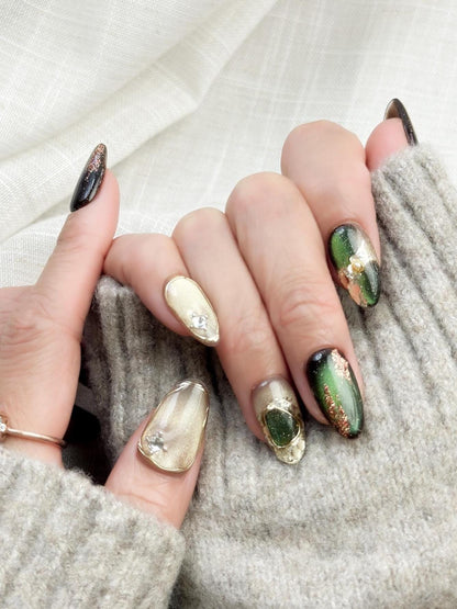 Hand with Green and gold gemstone-inspired press-on nails with cat-eye shimmer, glitter accents, gold foil detailing, and 3D crystal embellishments