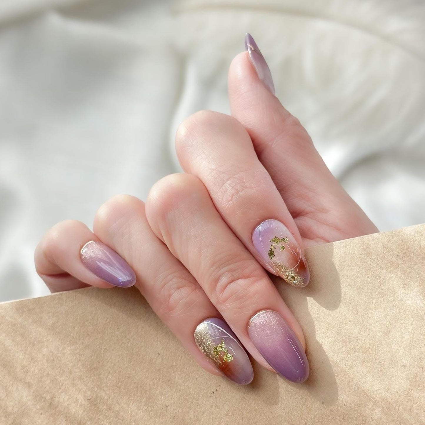 Almond shape purple press-on nails with gold foil accents and soft gradient shimmer. Elegant reusable salon-style press on nails by ManiFleur, featuring lavender ombré, metallic details, and glossy finish