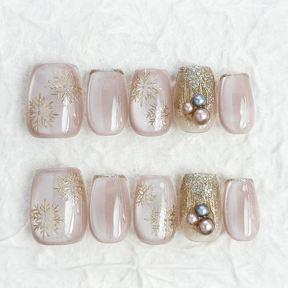 nude pink press-on nails with gold snowflake designs and glitter accents, featuring pearl embellishments for a festive holiday look