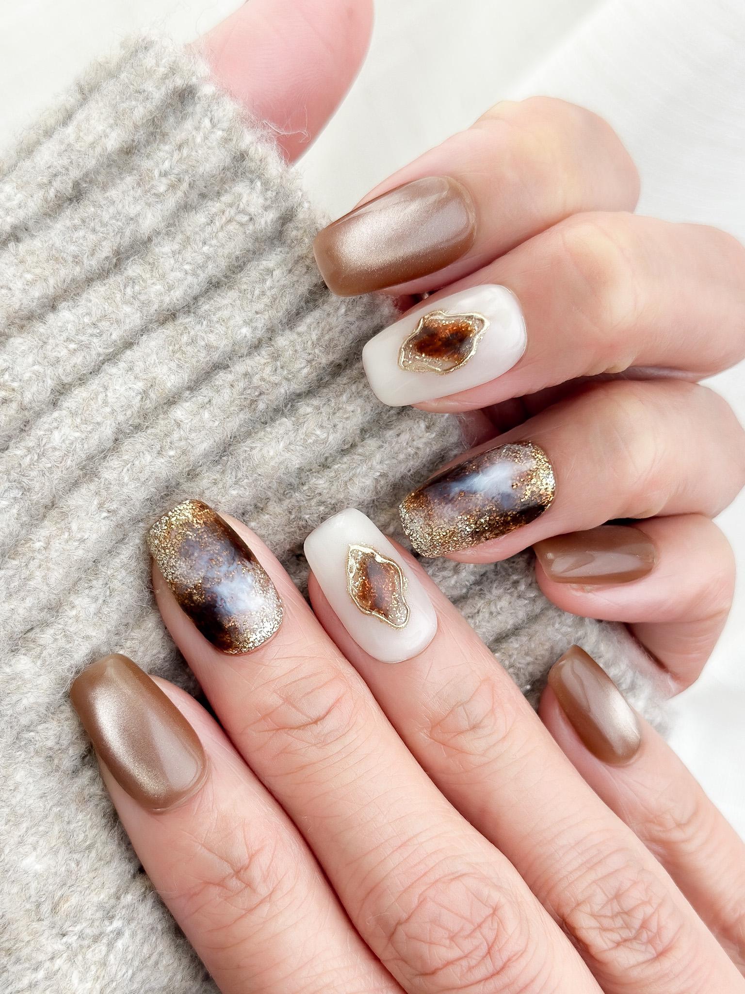 Hand with brown and ivory press-on nails in tortoise pattern, with gold foil detailing, and glossy cat-eye shimmer