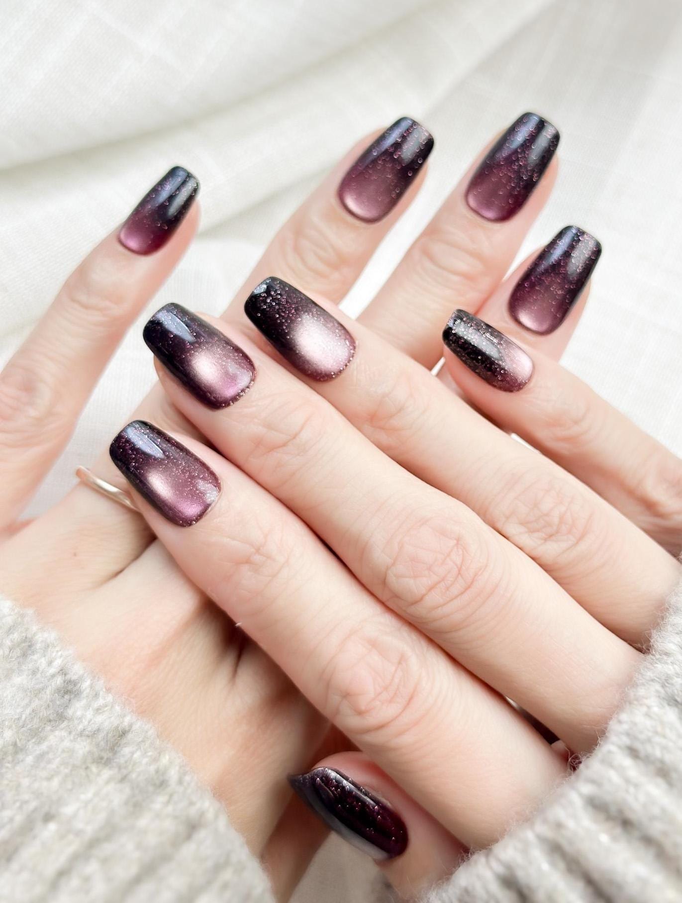Short square press-on nails in a deep plum purple cat-eye shimmer with black gradient edges and silver sparkle accents