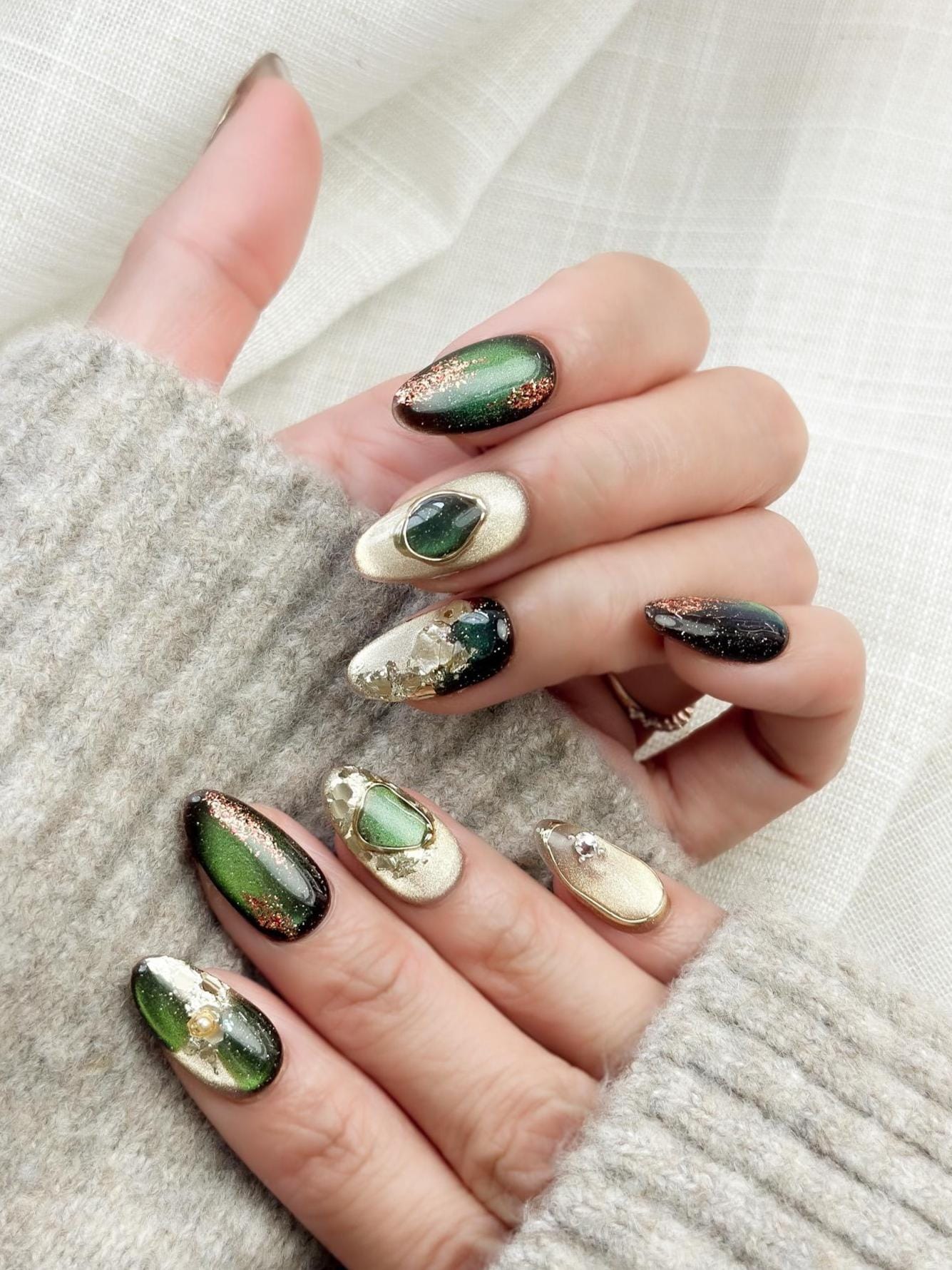 Green and gold gemstone-inspired press-on nails with cat-eye shimmer, glitter accents, gold foil detailing, and 3D crystal embellishments