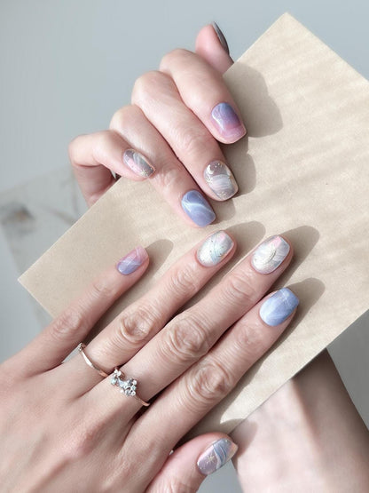 Hand with Pastel celestial press-on nails with pink, lavender, and blue marble swirls, gold star accents, and a gold crescent moon design