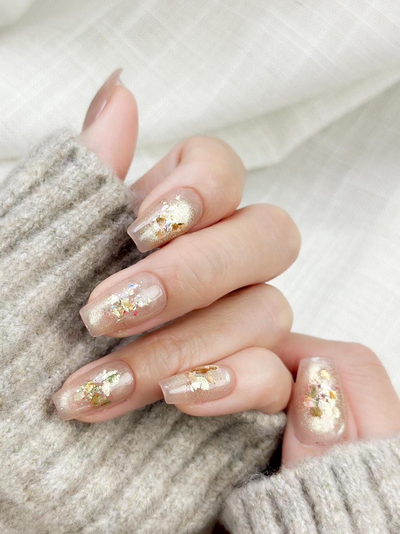 Hand showing press on nail with nude base and crushed foil glitter accent in gold
