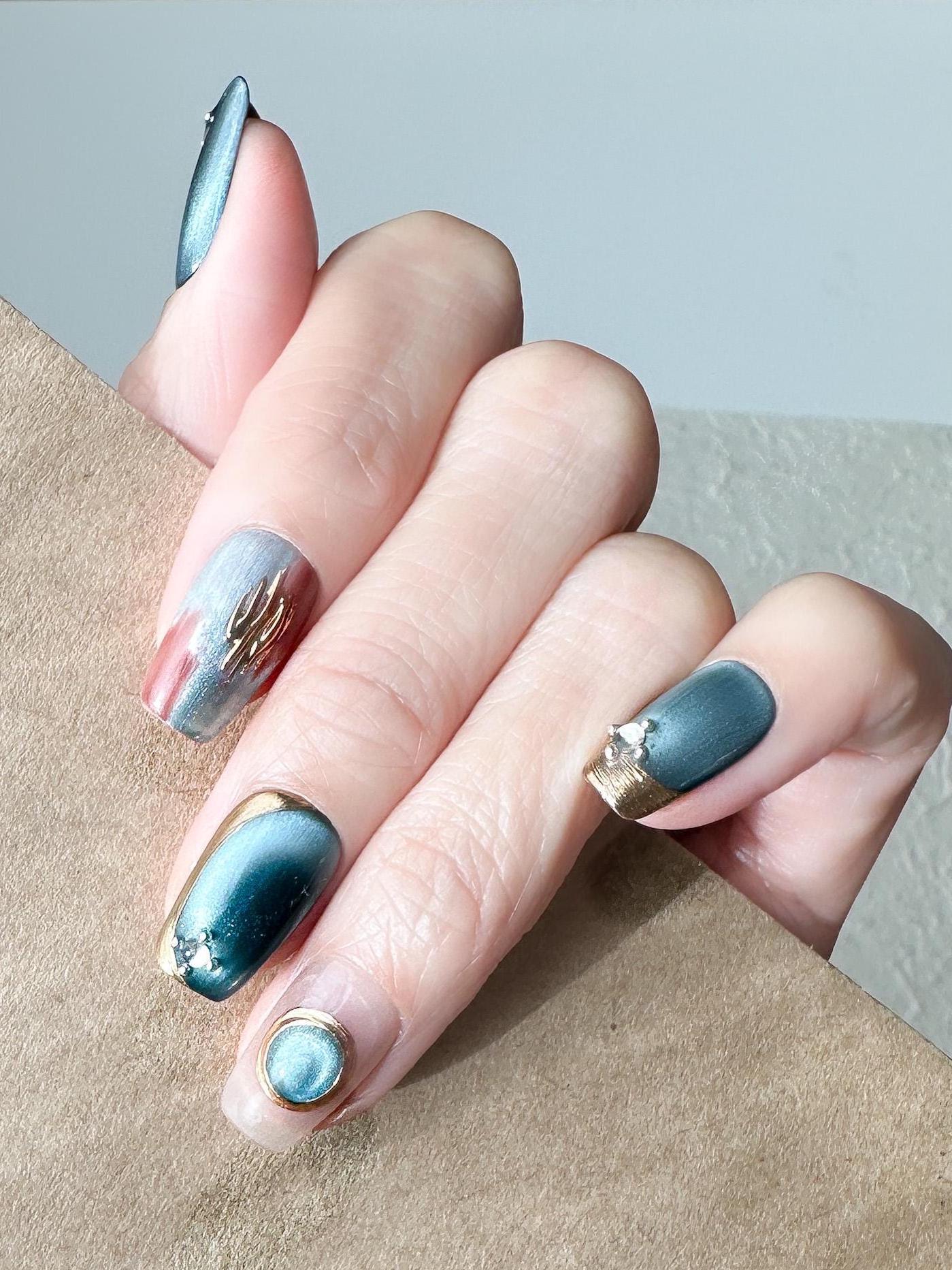 Close-up of deep blue and silver chrome press-on nails with gold accents and gemstone details, featuring a metallic cat-eye shimmer