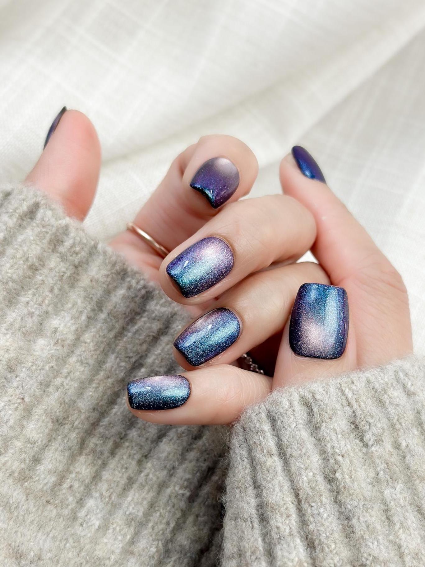Hand with Short square shaped cat-eye press-on nails in shifting blue, purple, and teal galaxy shimmer
