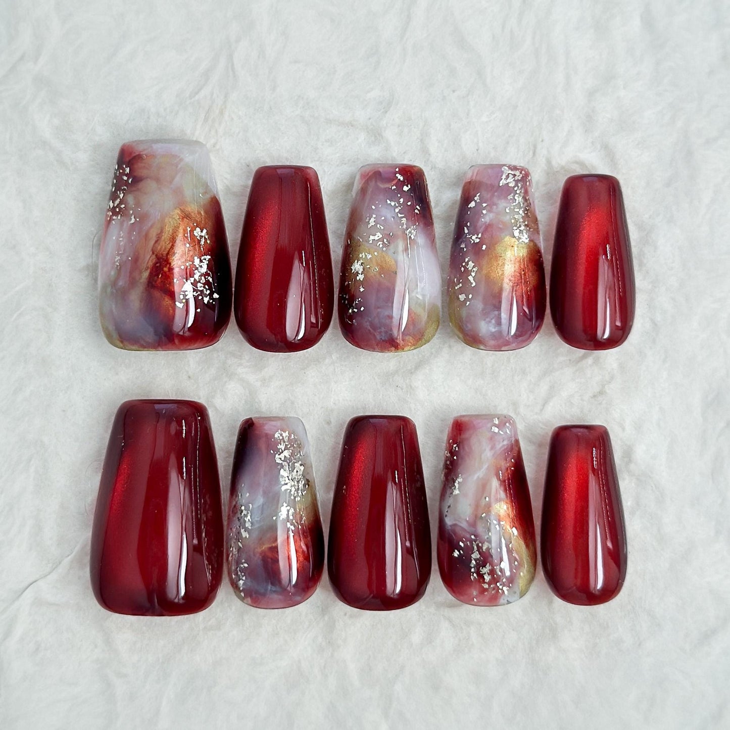 Press-on nails in deep burgundy red with multi-color abstract art accents marble effect and silver glitter details, festive holiday color