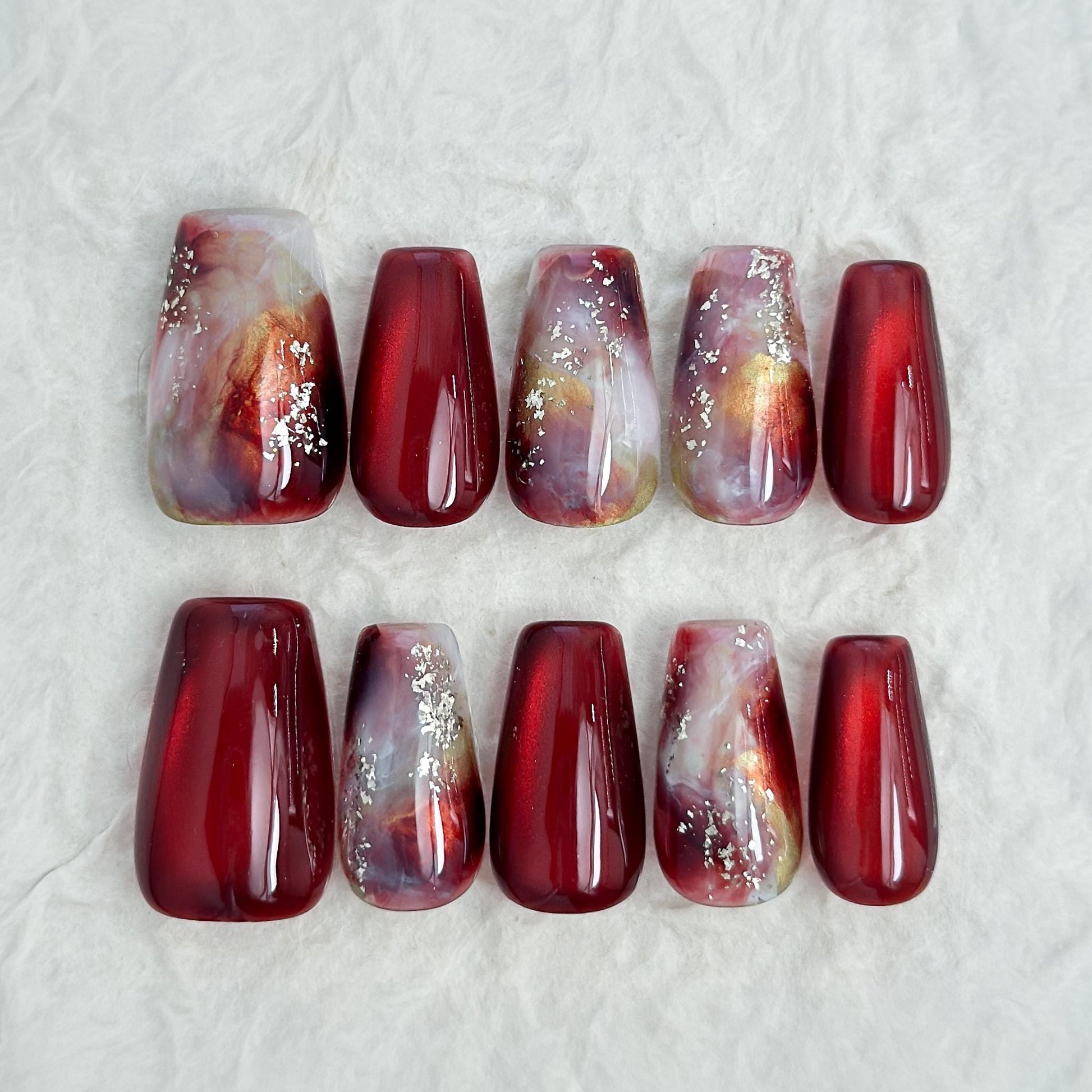 Press-on nails in deep burgundy red with multi-color abstract art accents marble effect and silver glitter details, festive holiday color