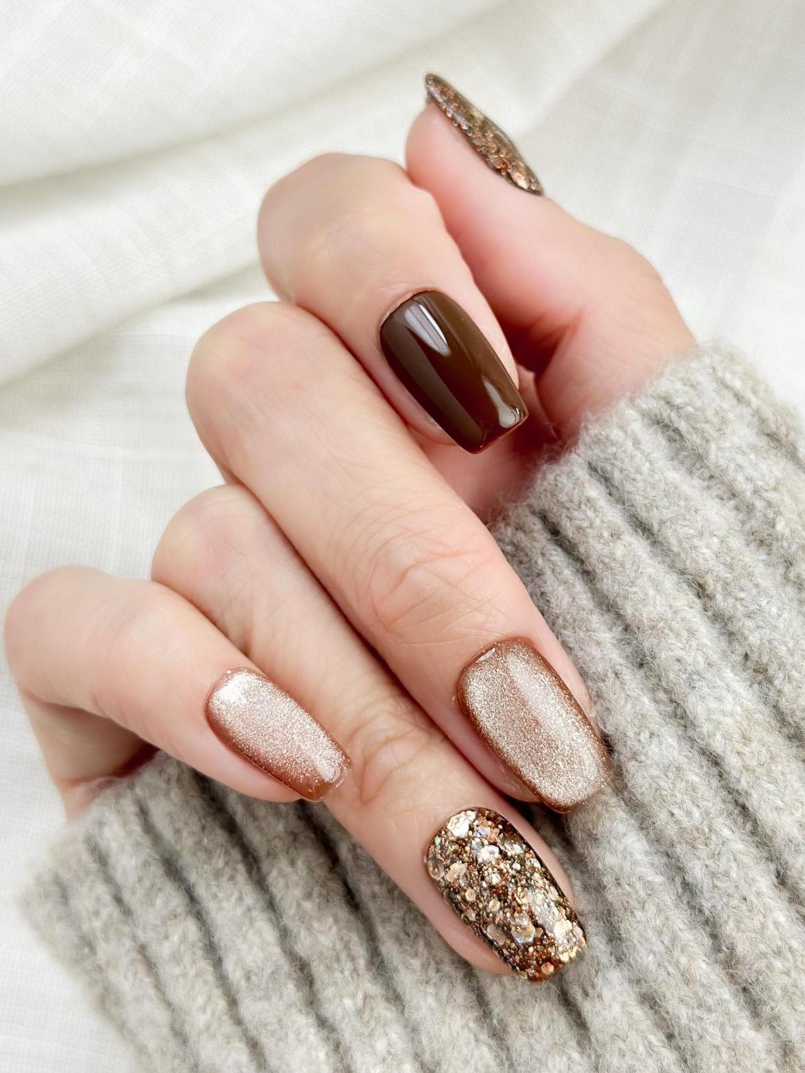 Hand with Brown and gold press-on nails with glossy chocolate brown polish, champagne shimmer, and gold glitter accent nails