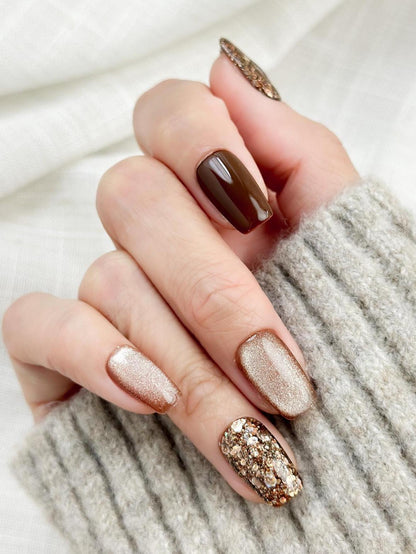 Hand with Brown and gold press-on nails with glossy chocolate brown polish, champagne shimmer, and gold glitter accent nails