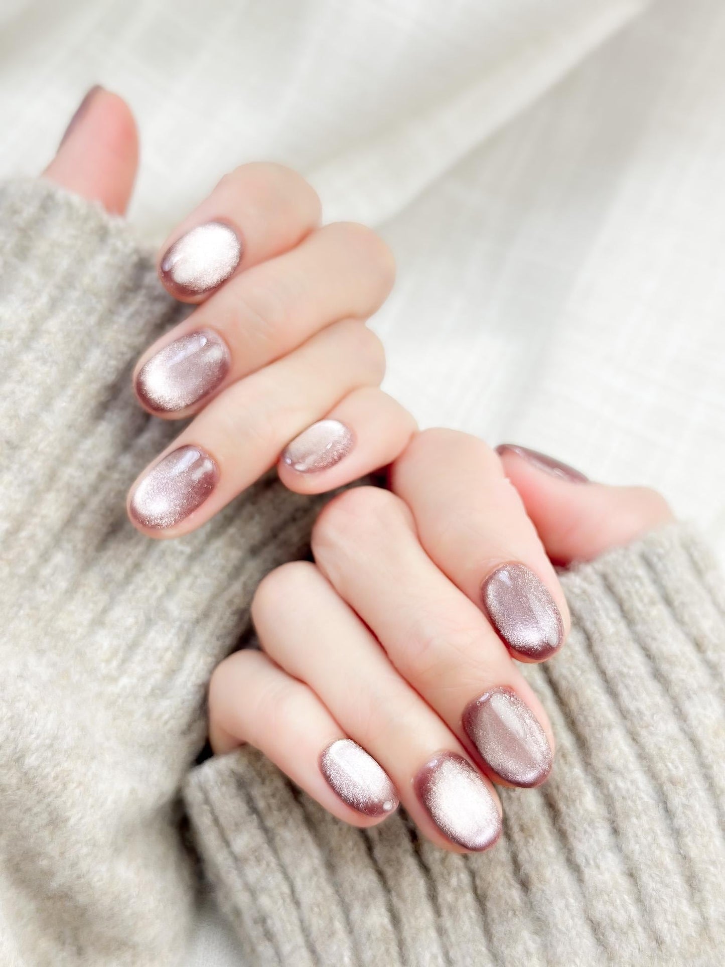 Short oval press-on nails in a metallic mauve cat-eye shimmer, glossy finish, luxury reusable press-on manicure by ManiFleur. Elegant mauve shimmer nails styled against a cozy knit sweater