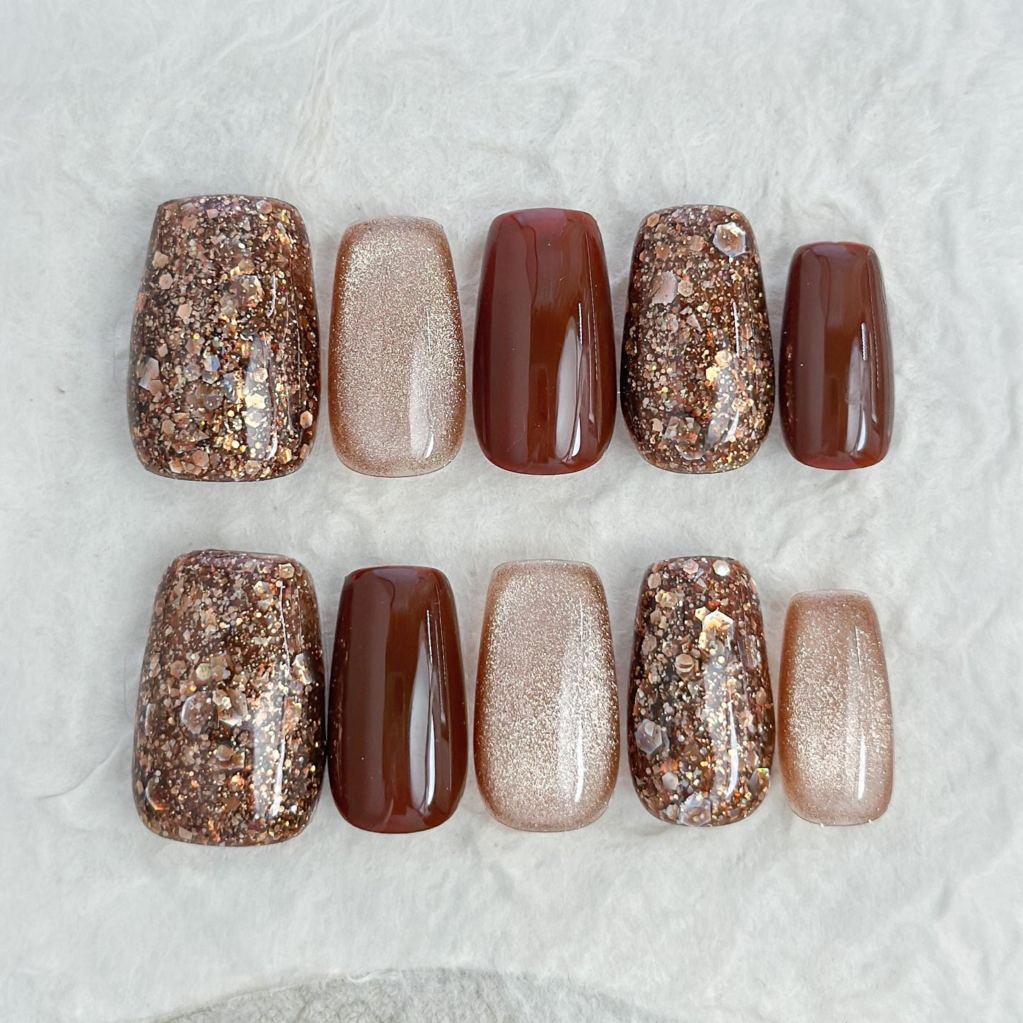 Brown and gold press-on nails with glossy chocolate brown polish, champagne shimmer, and gold glitter accent nails