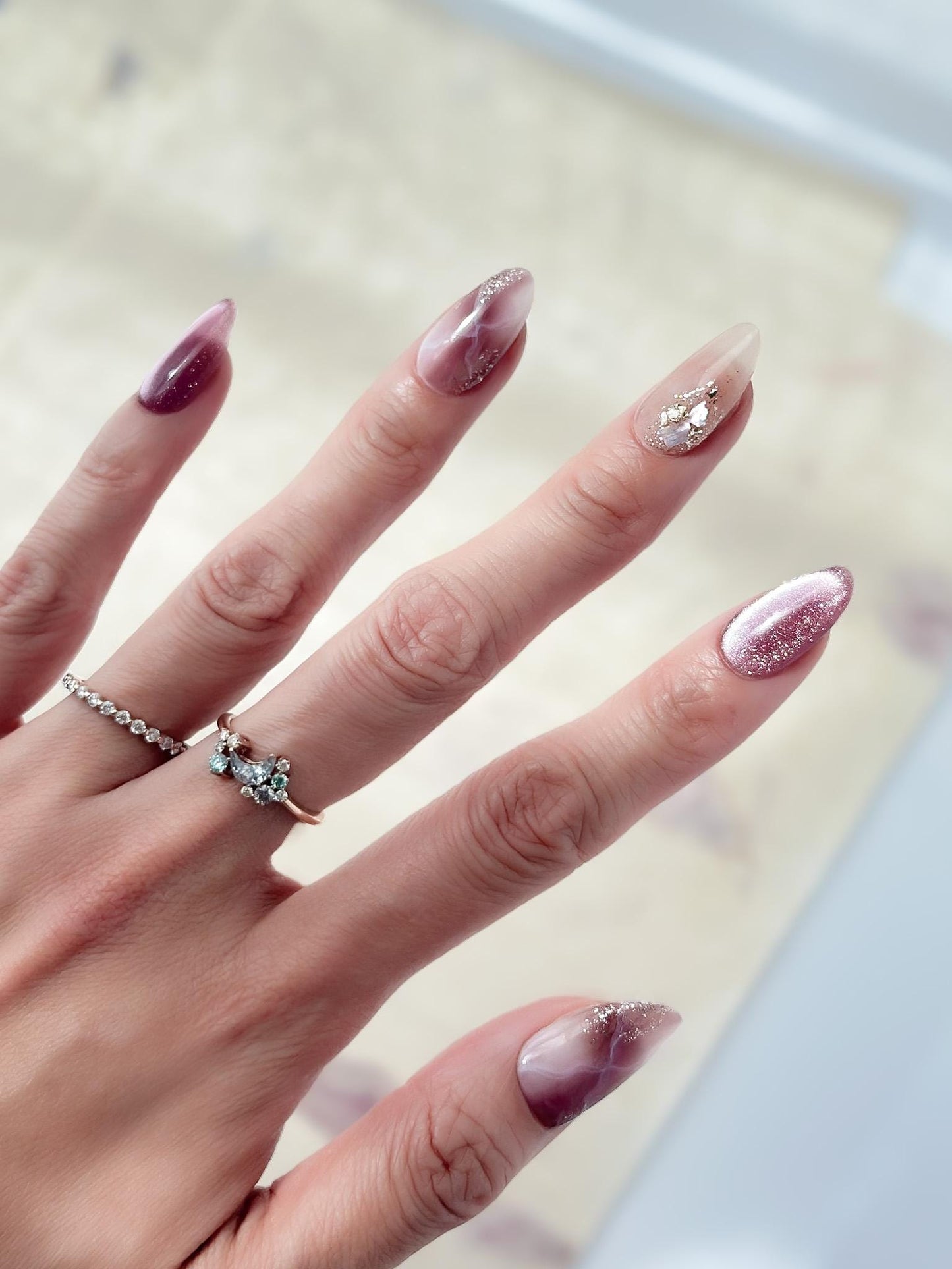 Hand with Pink and mauve press-on nails with marble design, cat eye shimmer finishes, and gold foil detailing