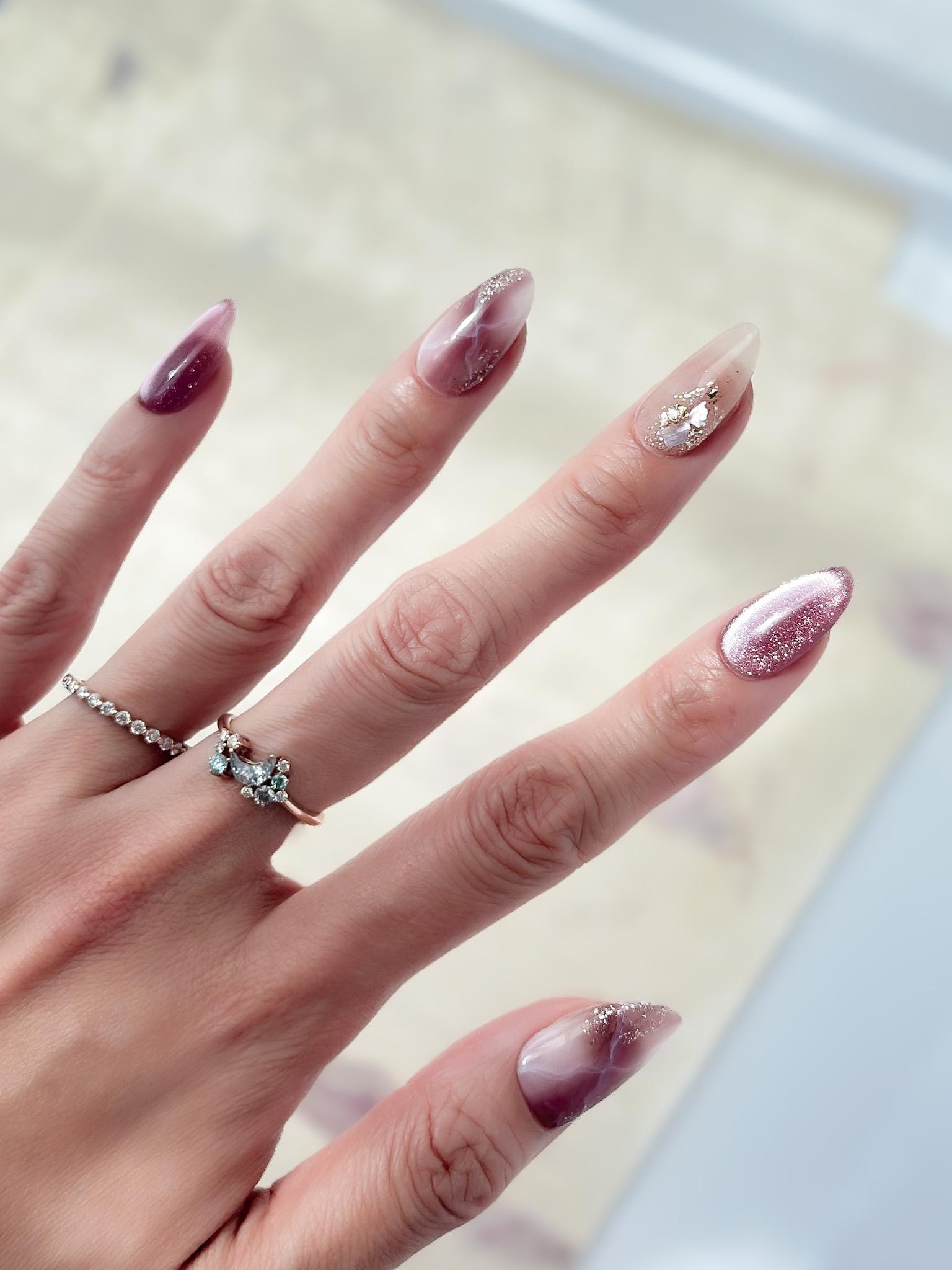 Hand with Pink and mauve press-on nails with marble design, cat eye shimmer finishes, and gold foil detailing