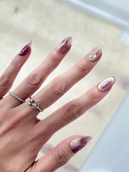Hand with Pink and mauve press-on nails with marble design, cat eye shimmer finishes, and gold foil detailing