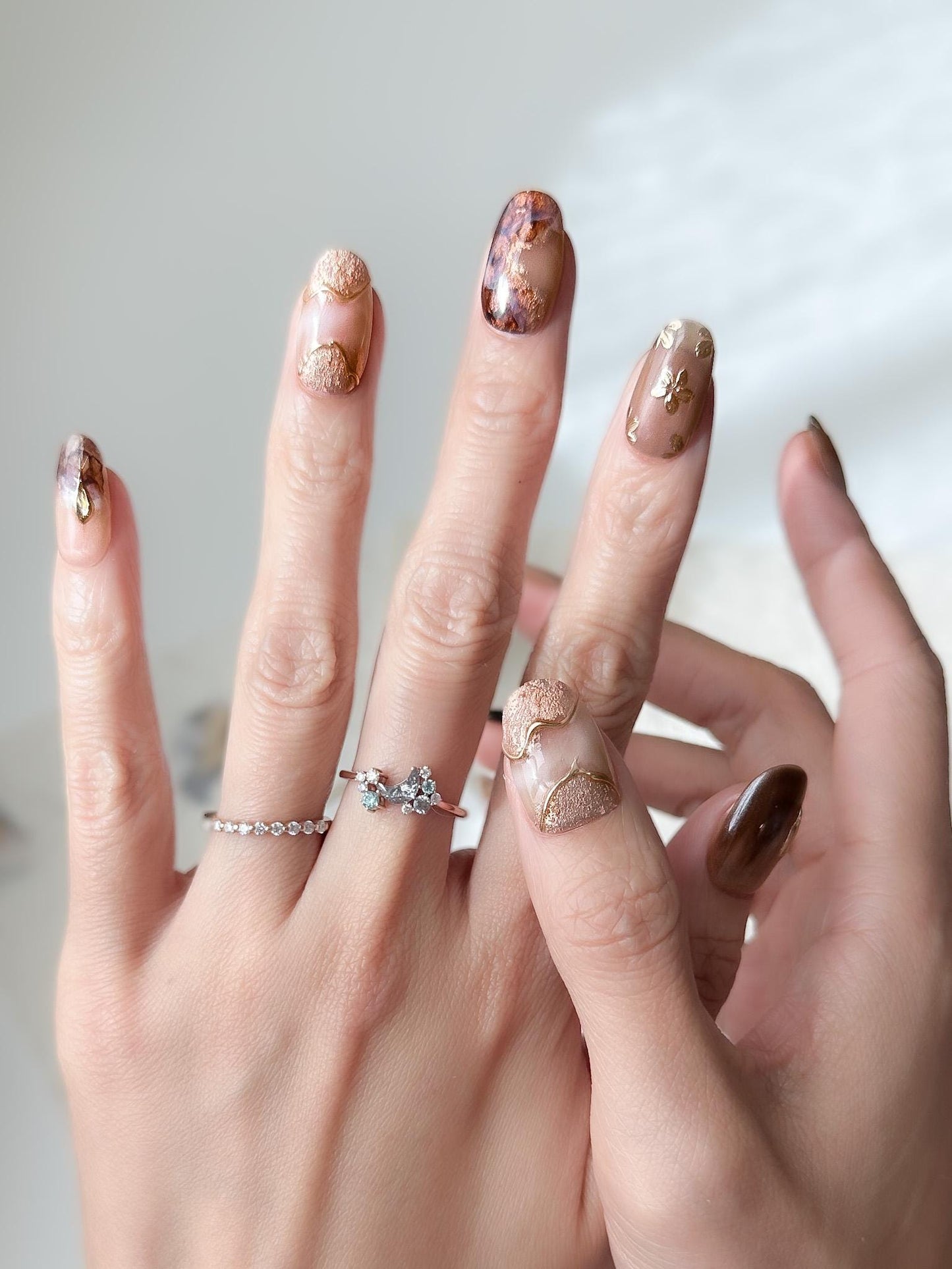 Hand with press-on nails in neutral tortoise design and mocha tones with gold foil accents, marble detailing, and embossed metallic floral designs