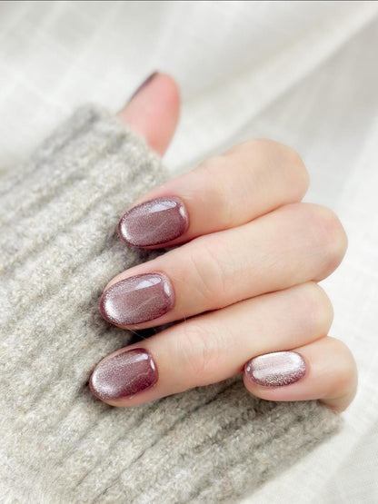 Short oval press-on nails in a metallic mauve cat-eye shimmer, glossy finish, luxury reusable press-on manicure by ManiFleur. Elegant mauve shimmer nails styled against a cozy knit sweater