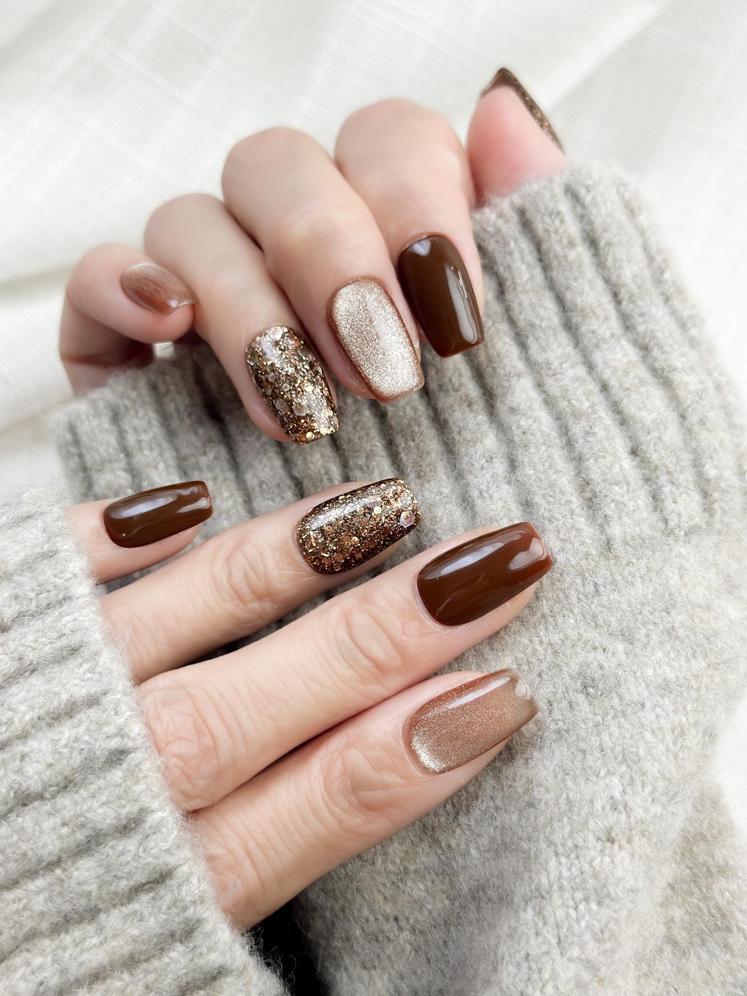 Hand with Brown and gold press-on nails with glossy chocolate brown polish, champagne shimmer, and gold glitter accent nails 