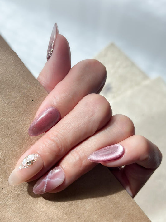 Hand with Pink and mauve press-on nails with marble design, cat eye shimmer finishes, and gold foil detailing.