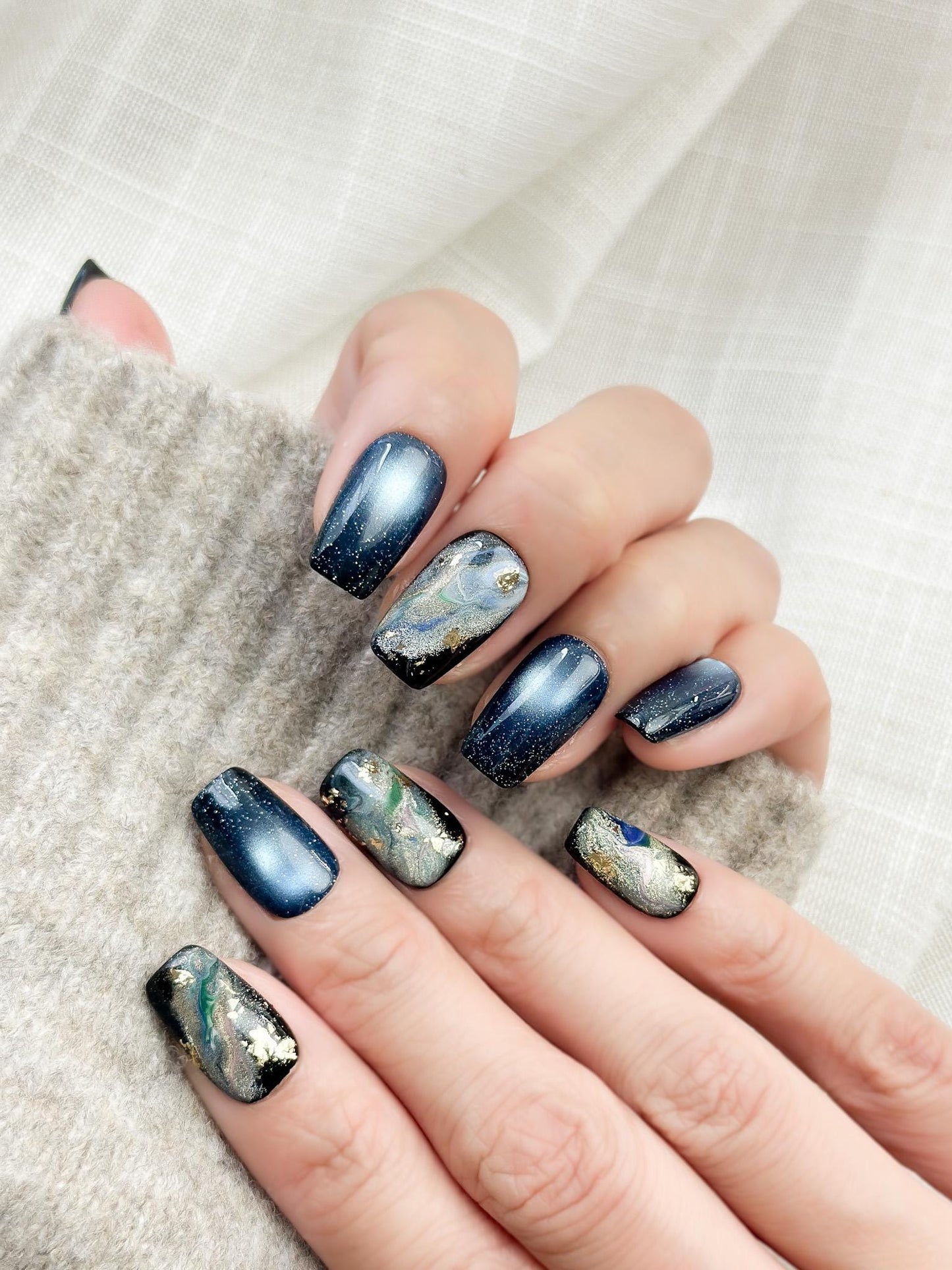Luxury blue cat-eye press-on nails with galaxy shimmer and abstract marble accents in green, gold, and silver foil