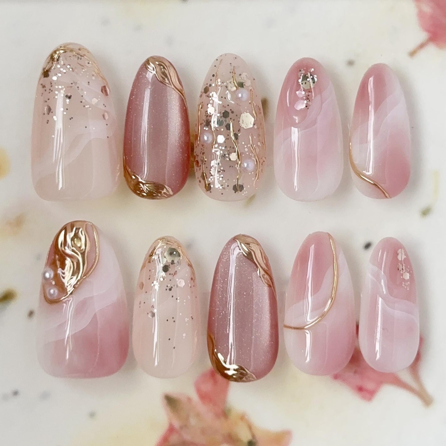 Set of Pink and nude luxury press-on nails with marble swirl designs, gold metallic accents, pearls, and glitter