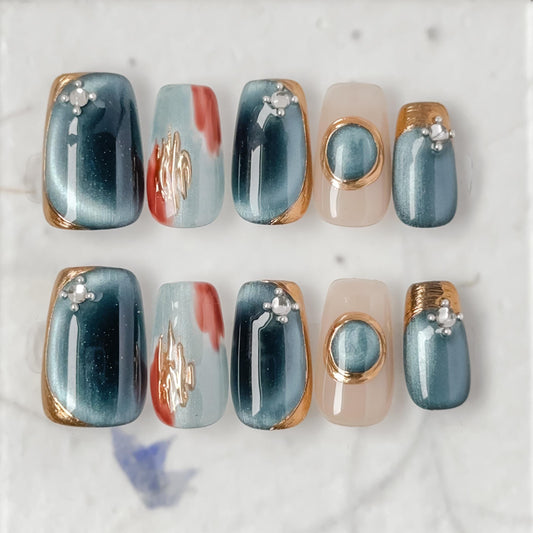 Close-up of deep blue and silver chrome press-on nails with gold accents and gemstone details, featuring a metallic cat-eye shimmer