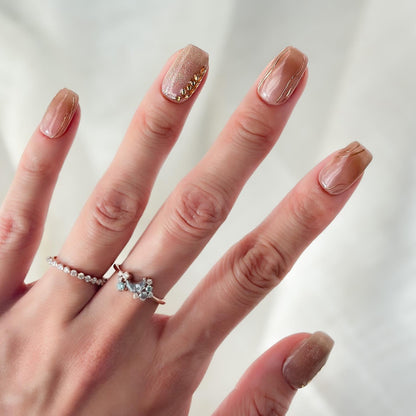Hand with Nude beige press-on nails with gold leaf accents and glossy marble lines. Elegant neutral nail set with gold embellishments