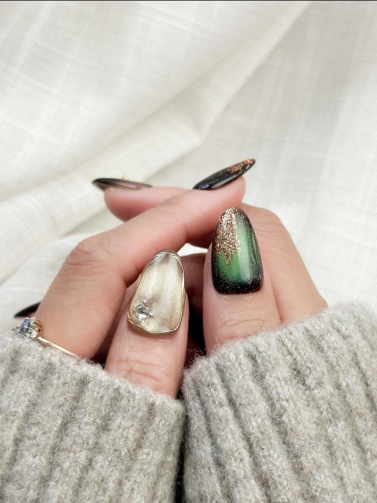 Green and gold gemstone-inspired press-on nails with cat-eye shimmer, glitter accents, gold foil detailing, and 3D crystal embellishments