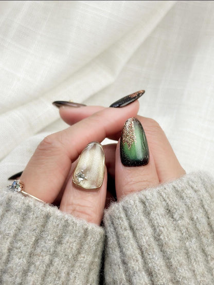 Green and gold gemstone-inspired press-on nails with cat-eye shimmer, glitter accents, gold foil detailing, and 3D crystal embellishments