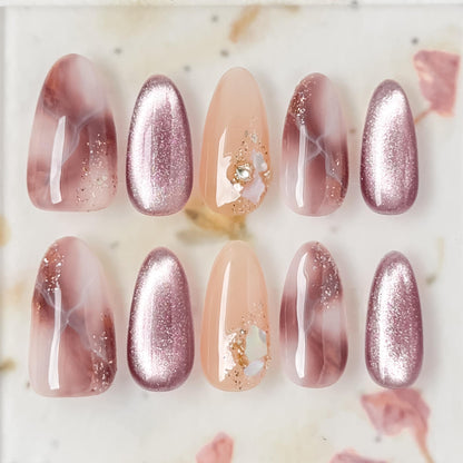 Pink and mauve press-on nails with marble design, cat eye shimmer finishes, and gold foil detailing