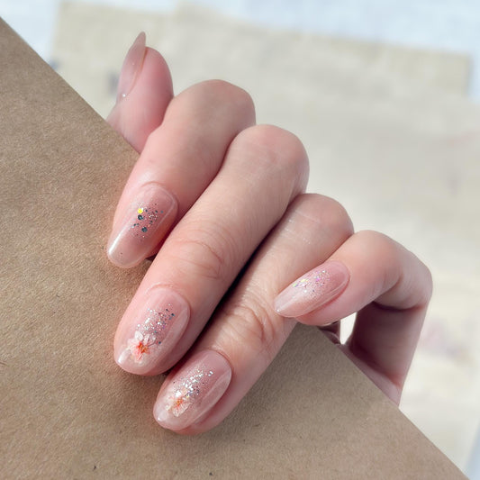 Hand with press on nail made with real dried flowers encased in a translucent blush base with fine glitter